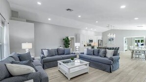 A modern living room with grey sofas, a white coffee table, and a kitchen in the background. - Coco Cobana - Heated Pool near Beach & Dining (Naples)