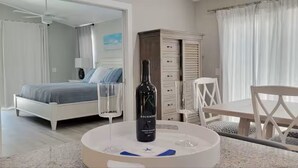 A bedroom with a bed, a bedside table with a bottle and glasses, a chair, and a wardrobe. - Coco Cobana - Heated Pool near Beach & Dining (Naples)