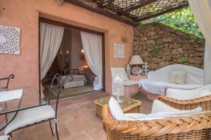 A cozy outdoor seating area with wicker furniture, a glass table, and a stone wall backdrop.