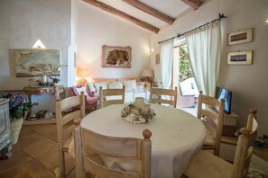 A dining area with a round table, wooden chairs, a chandelier, and a stone wall.