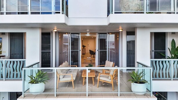 A modern two-story building with a balcony, large windows, and potted plants. - Stylish Apartment with City Views, Pool, and Walkable Cairns Location (Cairns City)