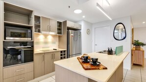 A modern kitchen with built-in appliances, a central island, and a dining area with a chair. - Stylish Apartment with City Views, Pool, and Walkable Cairns Location (Cairns City)