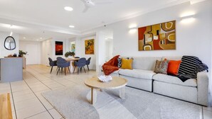 A modern living room with a sofa, coffee table, and dining area with chairs. - Stylish Apartment with City Views, Pool, and Walkable Cairns Location (Cairns City)