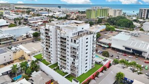 A high-rise building with multiple balconies, surrounded by other buildings and a beach in the background. - Stylish Apartment with City Views, Pool, and Walkable Cairns Location (Cairns City)