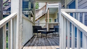 Una terraza de madera con dos sillas de mimbre y una escalera que conduce a un segundo piso.
