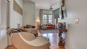 Una sala de estar moderna con un sofá, una silla de masaje, una mesa de centro y una escalera que sube a otro nivel.