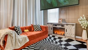 Una sala de estar con un sofá rojo, alfombra de estampado blanco y negro, chimenea y televisión montada en la pared.