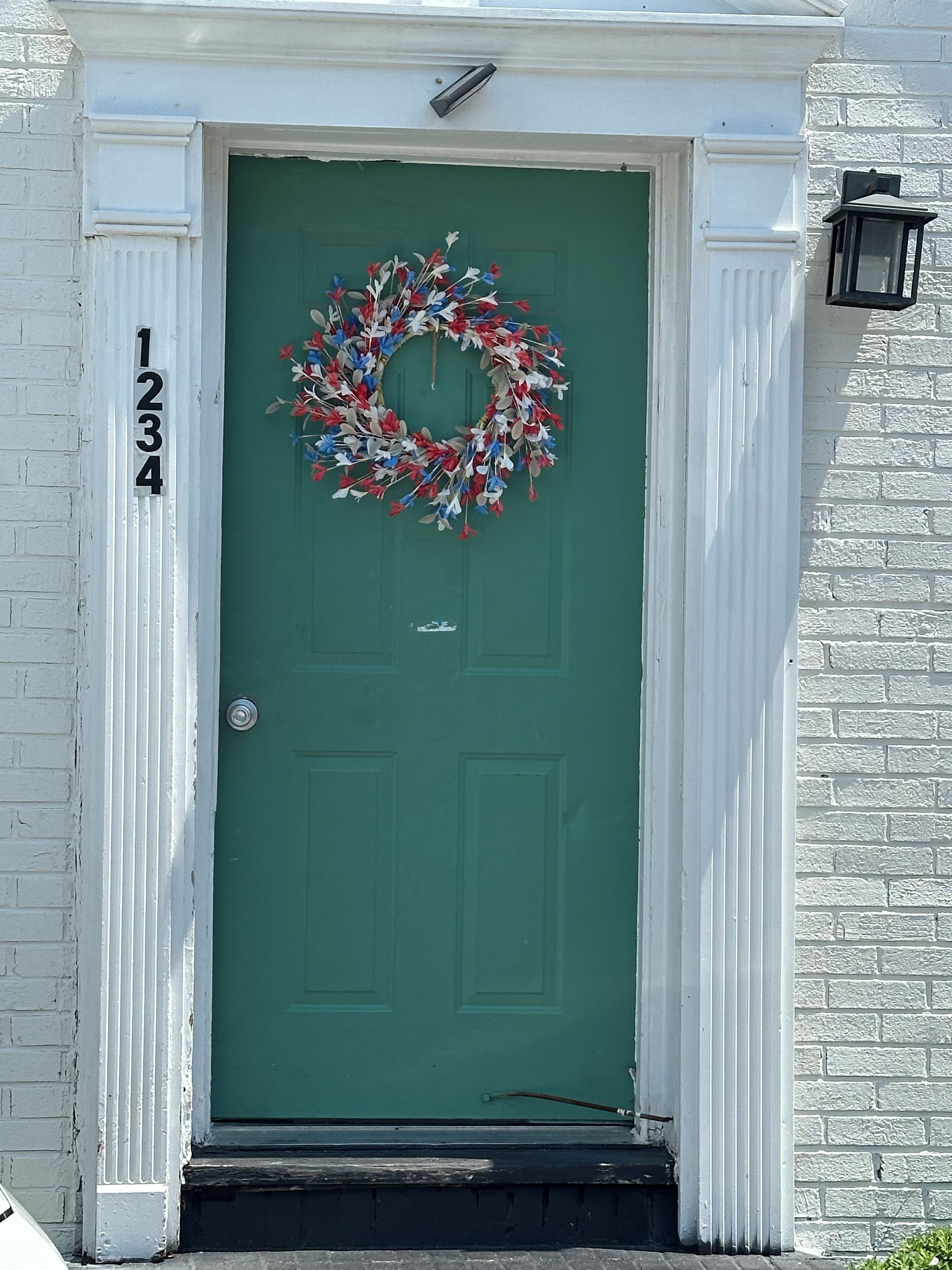 A green door with a wreath, a white door frame, and a number '1234' on the wall.