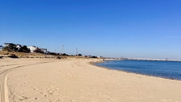 A sandy beach with footprints, a clear blue sky, and a distant pier.