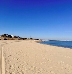 A sandy beach with footprints, a clear blue sky, and a distant pier.