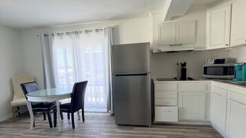 A modern kitchen with white cabinets, a stainless steel refrigerator, a microwave, and a dining area with a glass table and chairs.