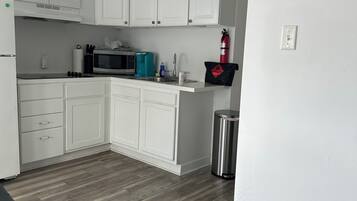 A compact kitchen with white cabinets, a microwave, a coffee maker, and a fire extinguisher.
