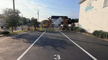 A parking lot with marked spaces, a building with a mural, and a gated entrance.