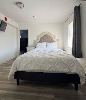 Un dormitorio con una cama, un televisor en la pared y una ventana con cortinas.