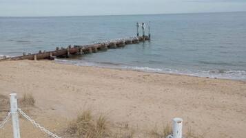 A beach with a chain-link fence and a wooden jetty extending into the water.