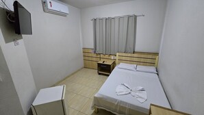 A small, clean room with a bed, a bedside table, a nightstand, a TV, and an air conditioning unit. - BRAVO CITY BIRIGUI (Birigui)