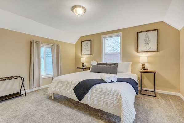 A bedroom with a large bed, two bedside tables with lamps, a radiator, and two framed pictures on the wall.
