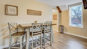 A dining area with a wooden table and four chairs, a framed artwork, a sign, and a window with blinds.