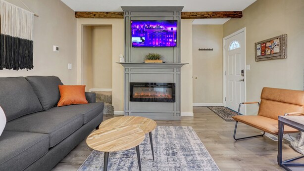 A living room with a gray sofa, a wooden coffee table, a fireplace, and a television mounted above it.