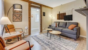 A modern living room with a grey sofa, orange cushions, a wooden coffee table, and a patterned rug.