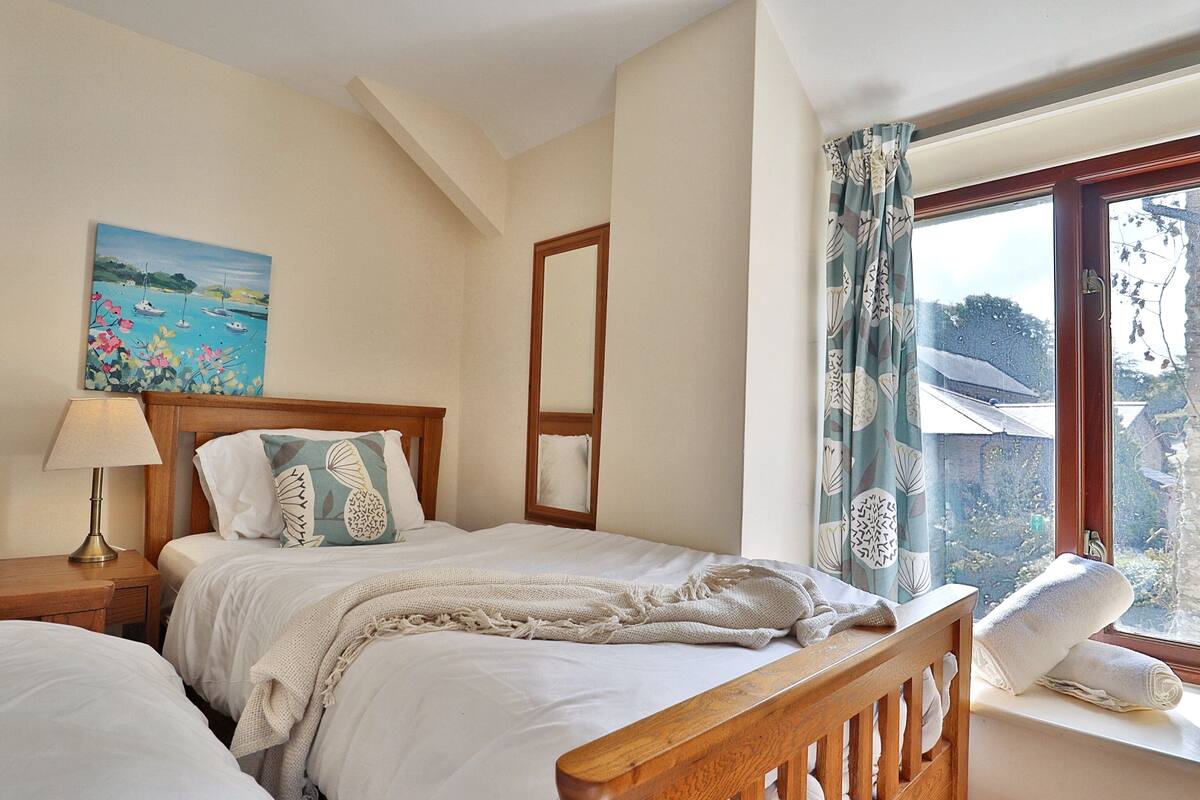 Ein Schlafzimmer mit zwei Betten, einem Bild an der Wand, einem Fenster mit Vorhängen und einem Holzkopfende.