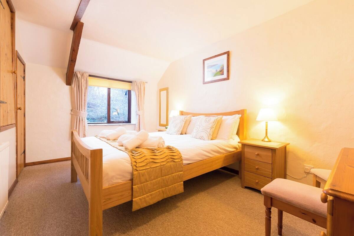 Ein gemütliches Schlafzimmer mit einem Holzbett, einem Nachttisch mit Lampe, einem Sessel und einem Fenster mit Vorhängen.