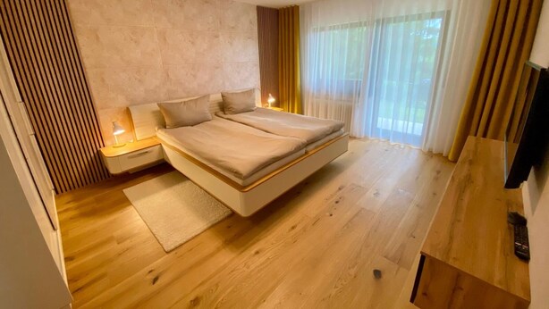 A modern bedroom with a large bed, bedside tables, a TV, and a window with curtains. - Candel view (Waldkirch)