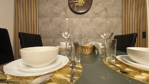 A dining table set with white plates, bowls, and cutlery, flanked by black chairs, with a decorative wall clock above. - Candel view (Waldkirch)