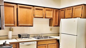 A kitchen with wooden cabinets, a white refrigerator, a dishwasher, and a sink. - Emerald Brick Home Downtown Indy (Indianapolis)