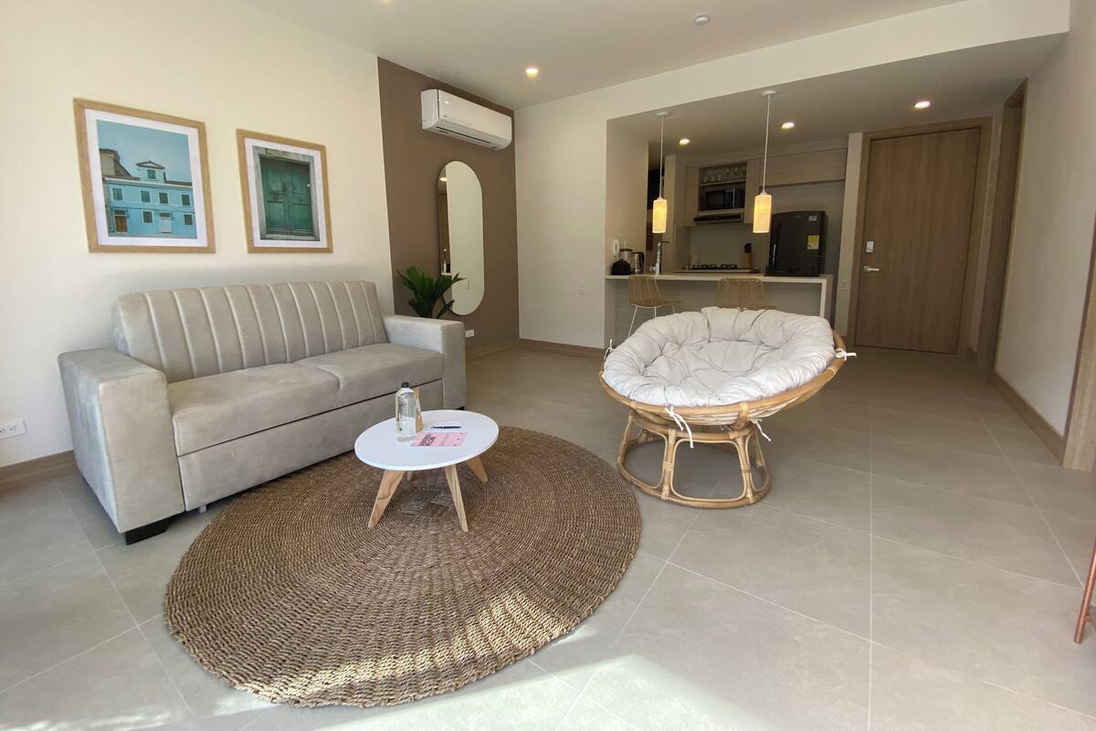 A living room with a sofa, a round coffee table, a wicker chair, and a large mirror.