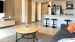 A modern living room with a round table, a grey sofa, and a kitchen area with a microwave and bar stools. - Morros Zoe by Wynwood House (Cartagena)