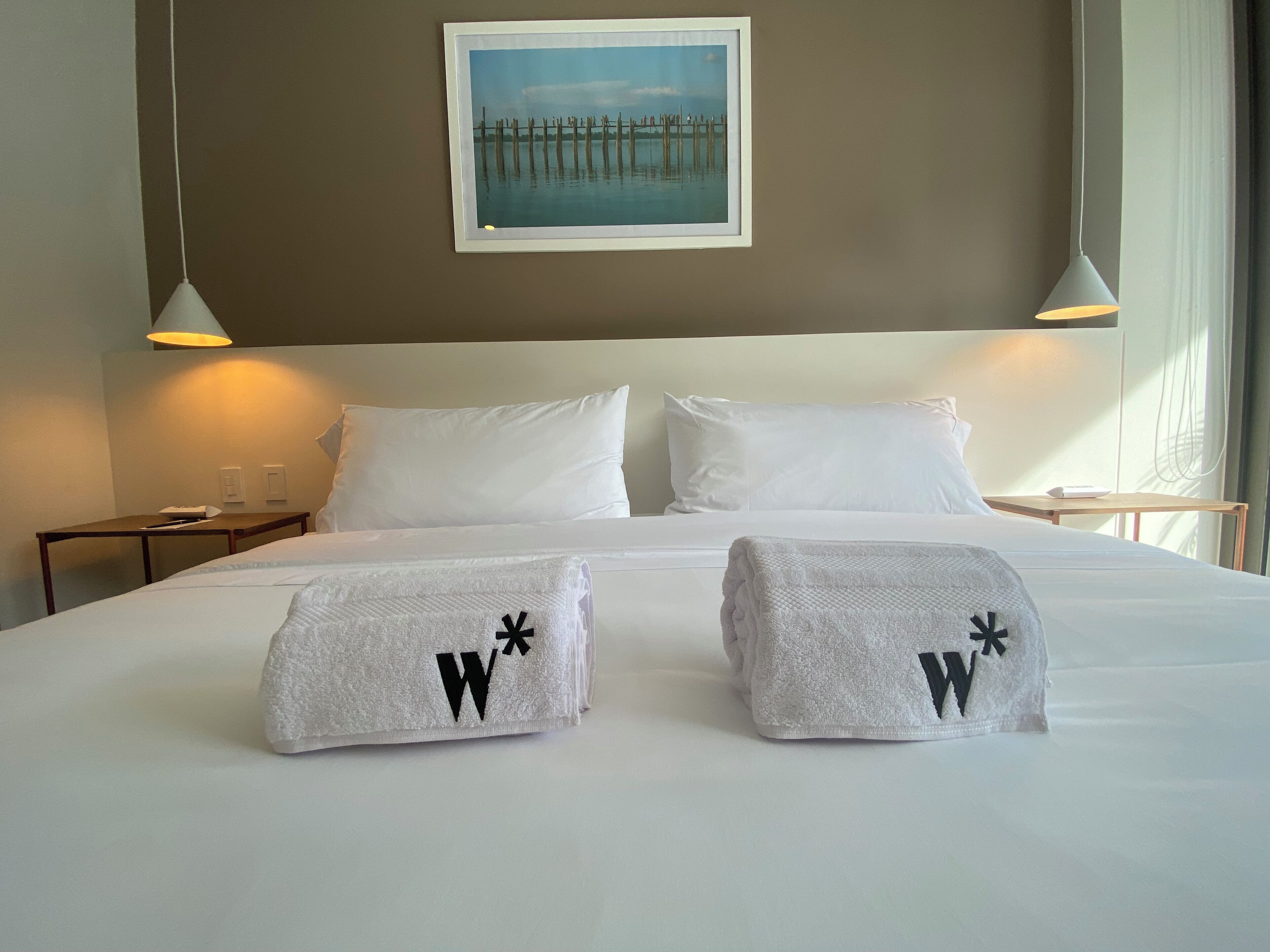 A hotel room with a large bed, two nightstands, a framed picture on the wall, and a window with curtains.