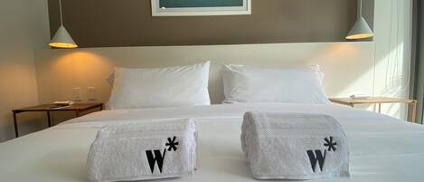 A hotel room with a large bed, two nightstands, a framed picture on the wall, and a window with curtains.