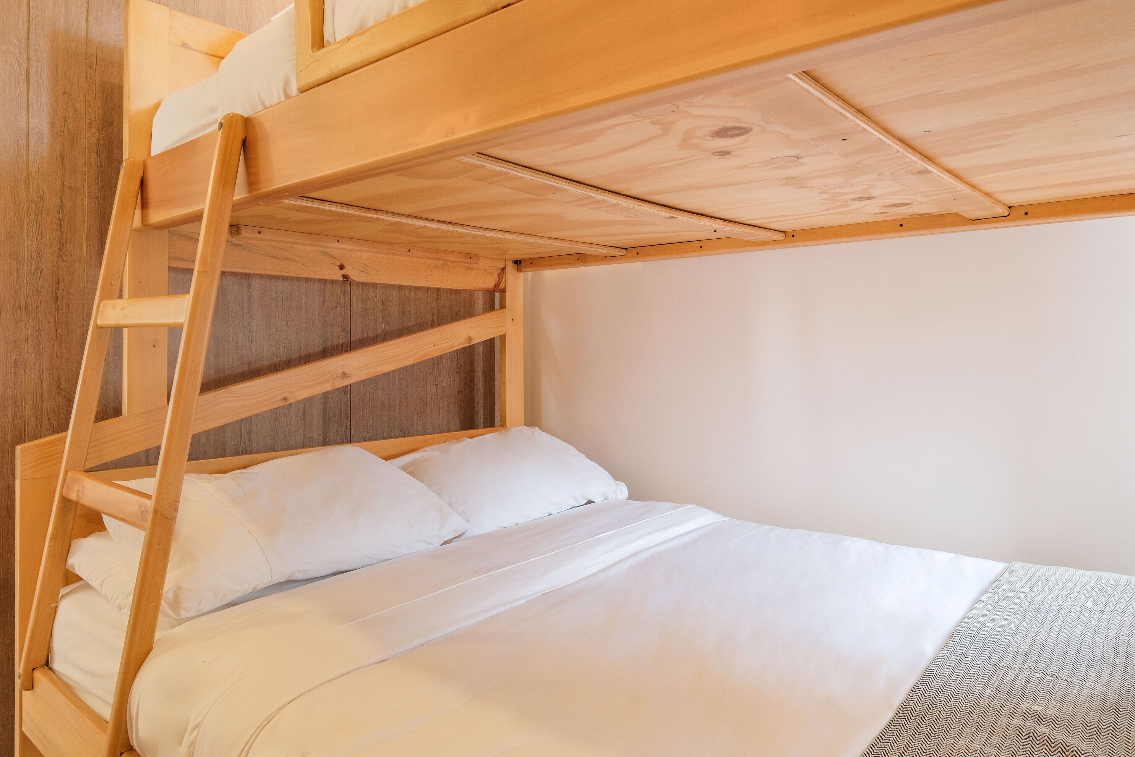 A bunk bed with white bedding and a wooden ladder.