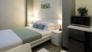 Hotellihuone, jossa on sänky, yöpöydät, mikroaaltouuni ja pieni jääkaappi.