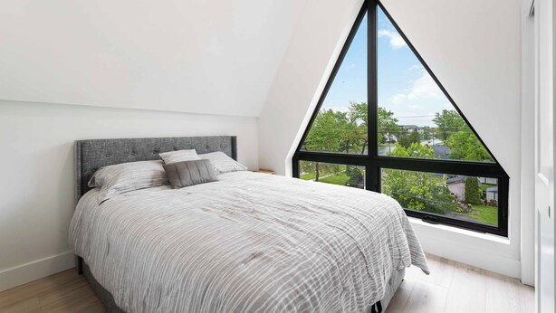 A bedroom with a large window, a bed with a grey headboard, and a view of greenery outside. - Modern/Spacious 2-story 2-bedrm. Free on-site parking. Near all things Niagara! (niagara falls)