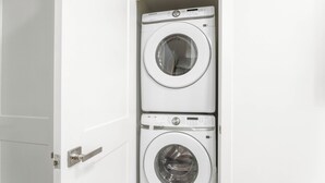 A white door with a silver handle leading to a laundry room containing two stacked front-loading washing machines. - Modern/Spacious 2-story 2-bedrm. Free on-site parking. Near all things Niagara! (niagara falls)