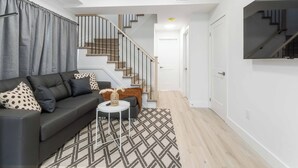 A modern living room with a grey sofa, patterned rug, and a staircase with wooden railings. - Modern/Spacious 2-story 2-bedrm. Free on-site parking. Near all things Niagara! (niagara falls)