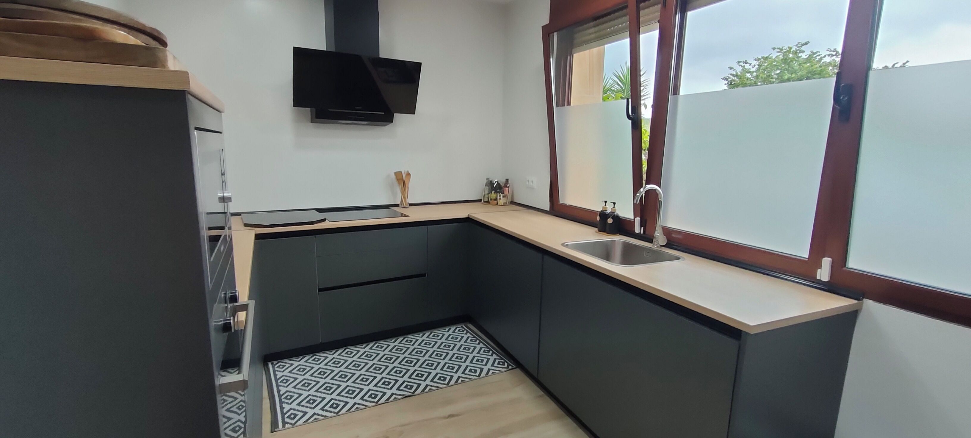 A compact kitchen with dark cabinetry, a built-in microwave, a stainless steel sink, and a window with a view of greenery outside.