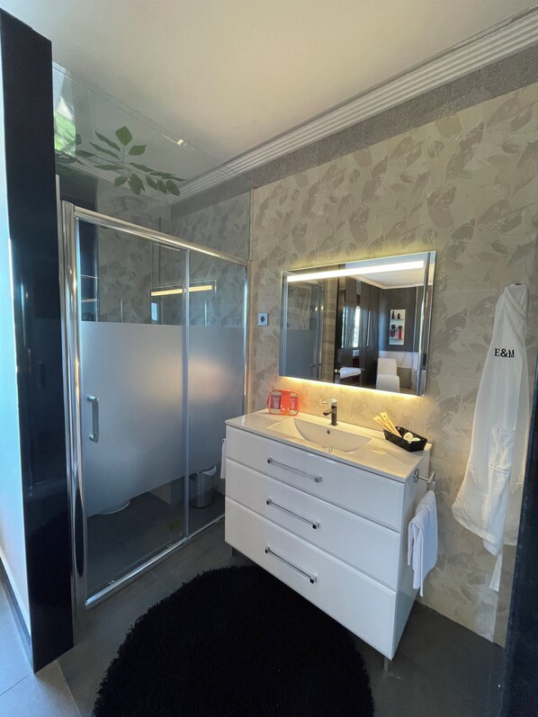 Un baño moderno con cabina de ducha de vidrio, tocador blanco con espejo y alfombra negra.