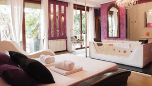 A modern bedroom with a large bed, a sitting area with a swing chair, a bathtub, and a large mirror. - Ebony & Ivory Suite Home. Probably One of a Kind in Spain (Camargo)