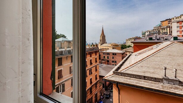 Une vue à travers une fenêtre sur un paysage urbain, avec des immeubles, le clocher d’une église et un ciel dégagé.
