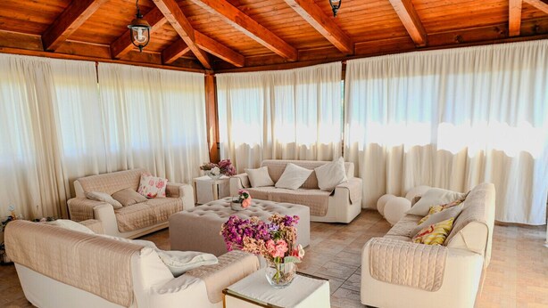 Un vaste espace de vie doté d’un plafond haut et de poutres en bois, comprenant plusieurs canapés et une table basse agrémentée d’un arrangement floral.