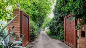 Un sentier bordé de murs de briques et d’une végétation luxuriante, qui mène à un petit bâtiment.