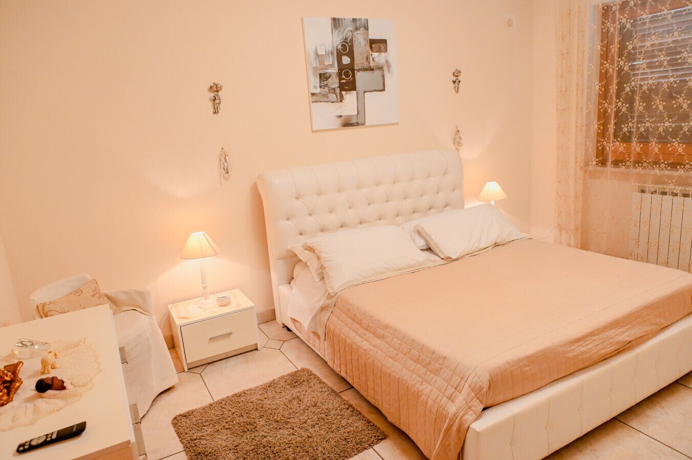 A bedroom with a large bed, two bedside tables, a nightstand, a rug, and a painting on the wall.