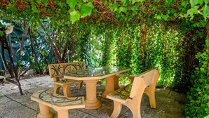 Une table et des chaises en pierre, disposées à l’extérieur, avec un décor de verdure en arrière-plan.