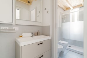 Une salle de bain avec un lavabo blanc, un miroir et une cabine de douche.