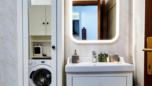 Ein kleines Badezimmer mit Waschmaschine, Waschbecken, Pflegeartikeln und einem Spiegel.