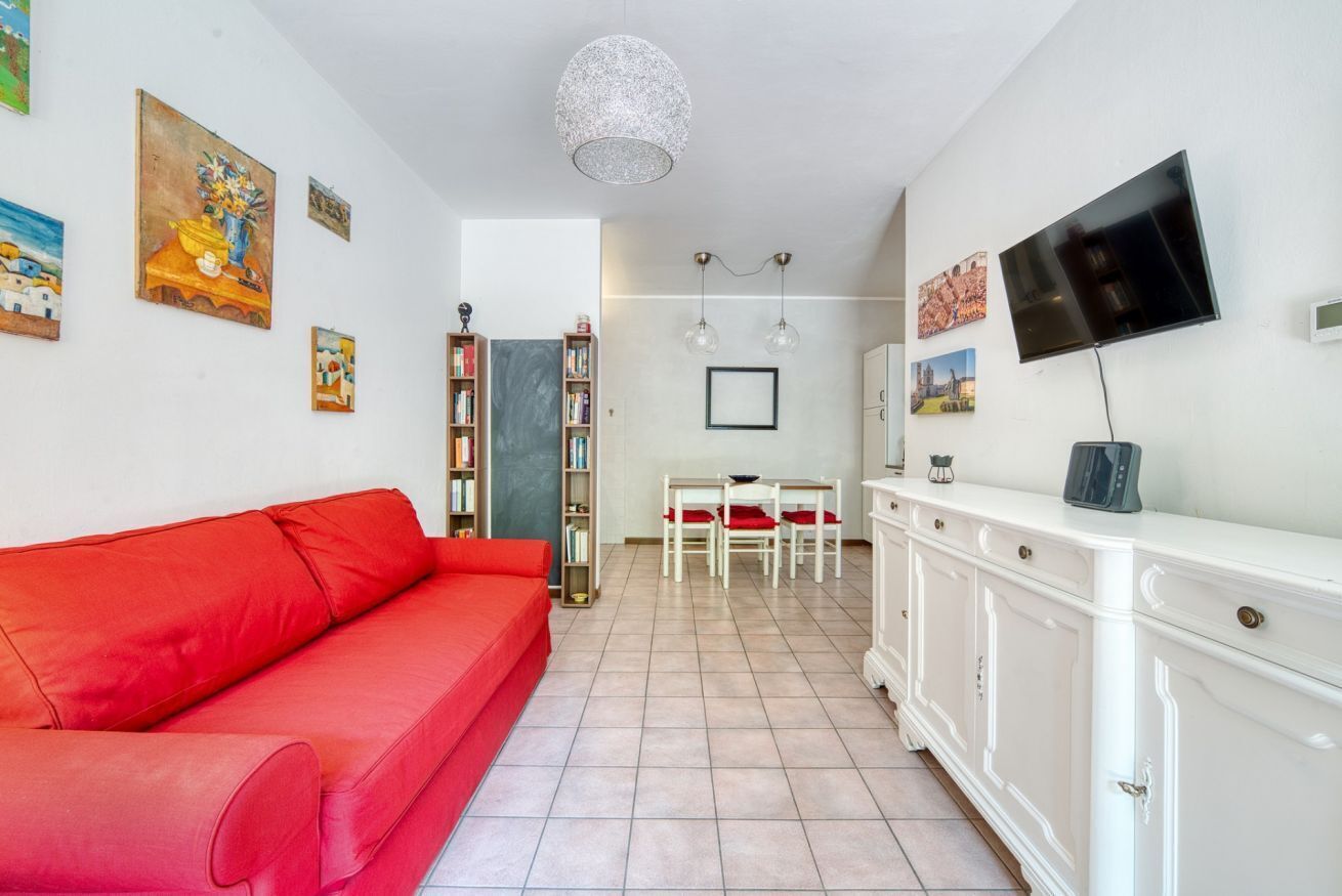 A living room with a red sofa, a white cabinet, a TV, and a dining area with chairs and a table.