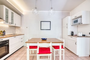 A modern kitchen with white cabinets, a wooden table, and red cushioned chairs.